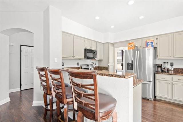 kitchen featuring dark stone counters, arched walkways, stainless steel refrigerator with ice dispenser, and black microwave