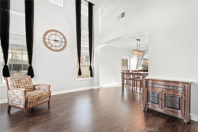 sitting room with visible vents, baseboards, a high ceiling, arched walkways, and dark wood-style flooring