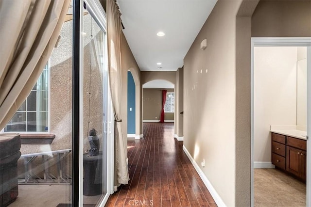 corridor featuring arched walkways, recessed lighting, baseboards, and wood finished floors