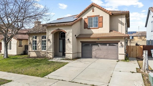 mediterranean / spanish-style home featuring solar panels, fence, concrete driveway, a front yard, and stucco siding