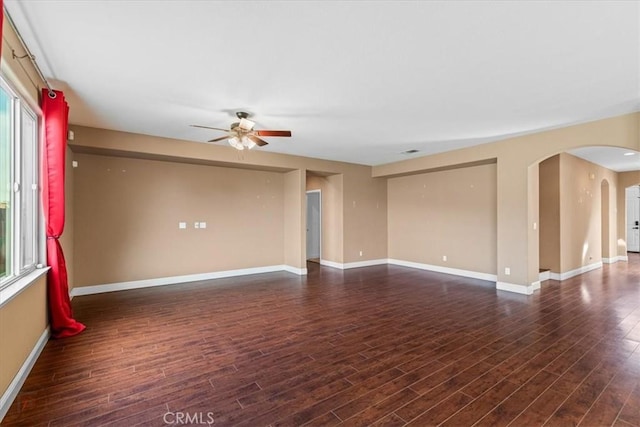 unfurnished room with arched walkways, baseboards, ceiling fan, and dark wood-style flooring