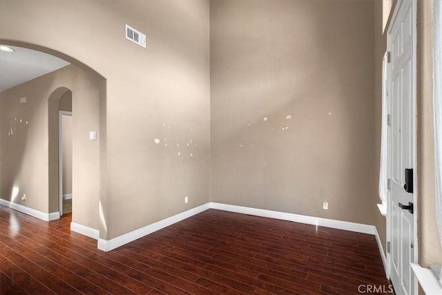 unfurnished room with visible vents, arched walkways, baseboards, and dark wood-style flooring