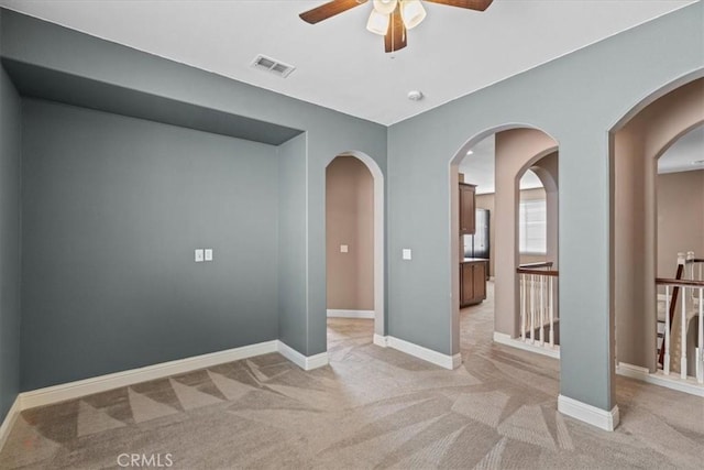 empty room featuring visible vents, light carpet, baseboards, and a ceiling fan