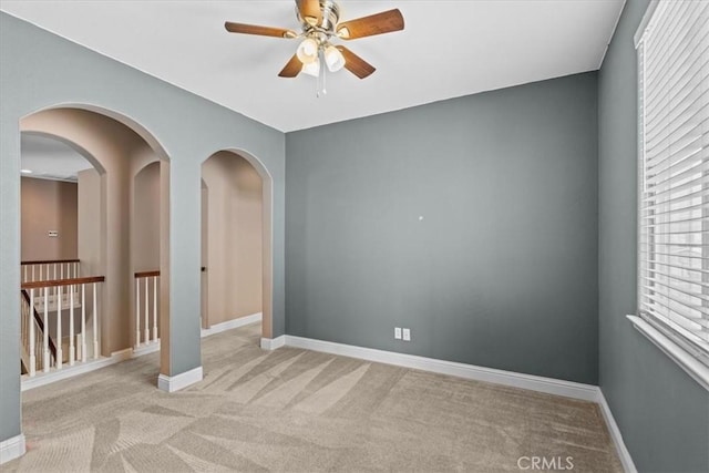 unfurnished room with ceiling fan, arched walkways, baseboards, and light carpet