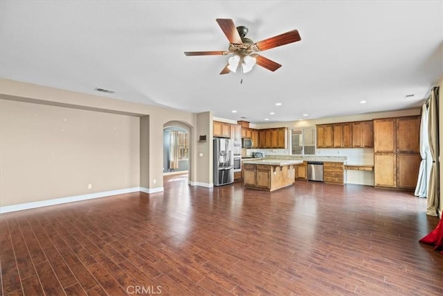 unfurnished living room with a ceiling fan, dark wood-type flooring, baseboards, and arched walkways