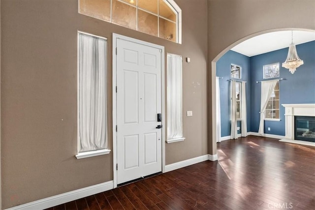 foyer entrance featuring a glass covered fireplace, wood finished floors, baseboards, and arched walkways