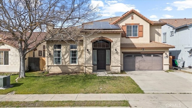 mediterranean / spanish-style home featuring stucco siding, driveway, roof mounted solar panels, a front yard, and a tiled roof