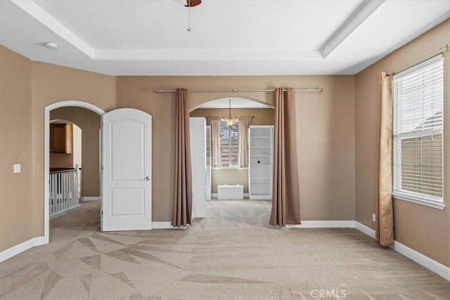 spare room featuring arched walkways, light colored carpet, and a tray ceiling