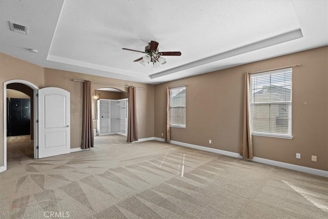 spare room featuring a tray ceiling, arched walkways, and visible vents