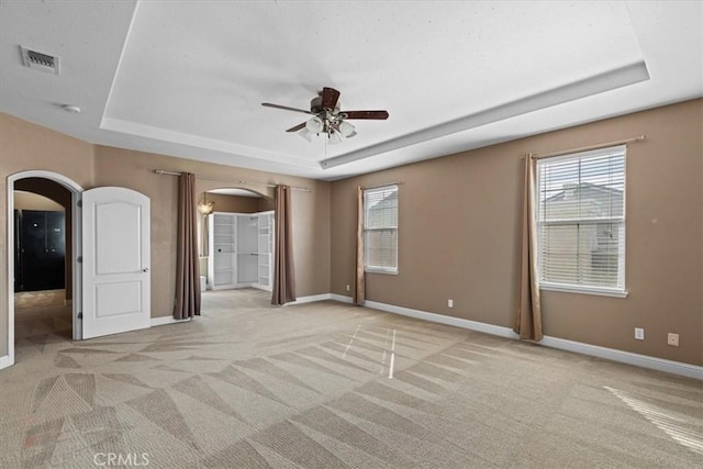 unfurnished bedroom featuring arched walkways, visible vents, baseboards, and a tray ceiling