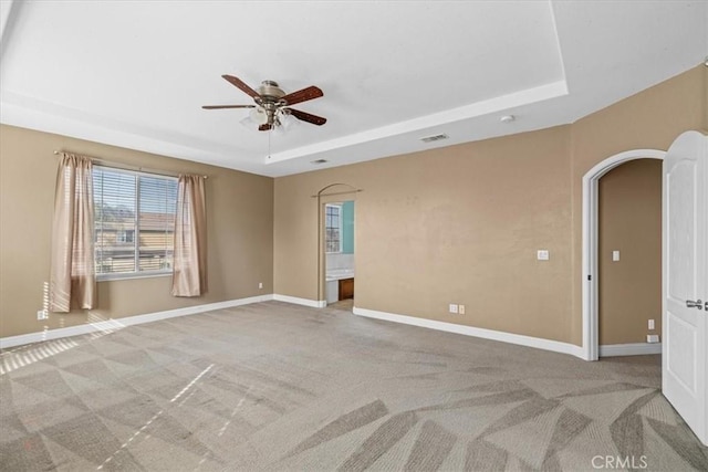 empty room with a raised ceiling, baseboards, arched walkways, and light carpet