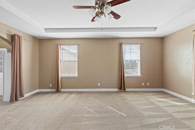 carpeted spare room featuring ceiling fan, baseboards, and a tray ceiling