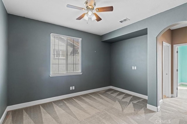 carpeted empty room with visible vents, arched walkways, baseboards, and ceiling fan