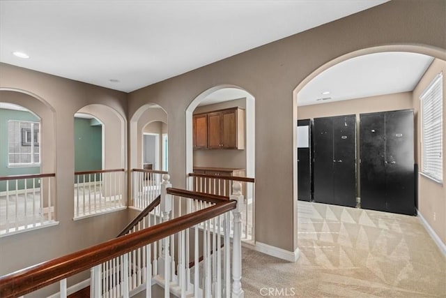 hallway featuring an upstairs landing, light colored carpet, and baseboards