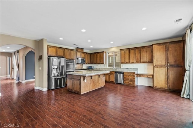 kitchen featuring a center island, light countertops, dark wood-style floors, arched walkways, and stainless steel appliances