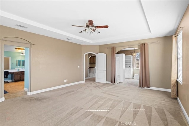 unfurnished room featuring visible vents, light carpet, a ceiling fan, a tray ceiling, and arched walkways
