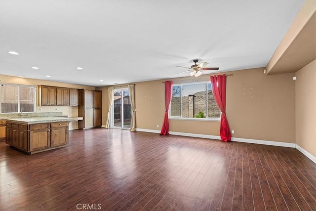 unfurnished living room featuring dark wood finished floors, a sink, baseboards, and ceiling fan