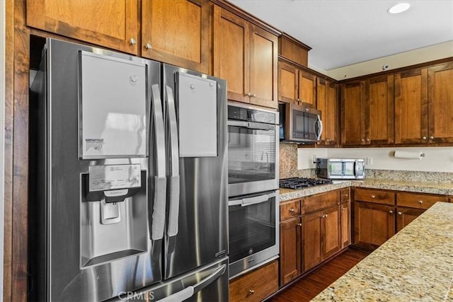 kitchen with light stone counters, recessed lighting, brown cabinetry, stainless steel appliances, and dark wood-style flooring