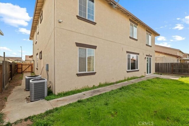 rear view of property featuring a gate, a fenced backyard, central AC, stucco siding, and a lawn