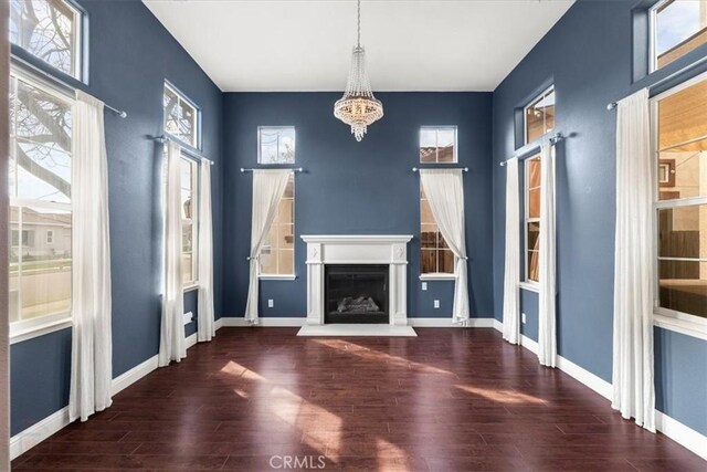 unfurnished living room featuring a fireplace with raised hearth, wood finished floors, baseboards, and a chandelier