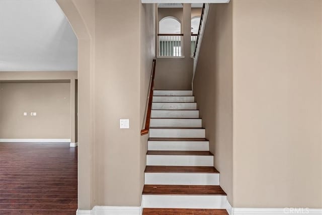 staircase with arched walkways, baseboards, and wood finished floors