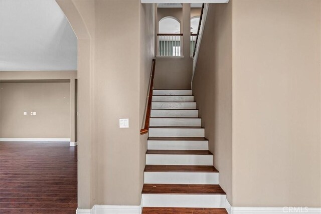 stairway featuring wood finished floors, baseboards, and arched walkways