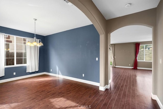 spare room with baseboards, arched walkways, an inviting chandelier, and wood finished floors