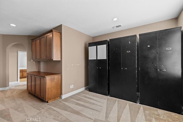 kitchen featuring visible vents, arched walkways, light colored carpet, and baseboards