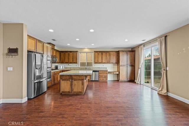 kitchen with brown cabinetry, baseboards, a kitchen island, dark wood-type flooring, and appliances with stainless steel finishes