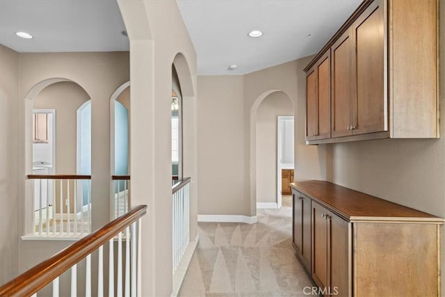 hallway featuring arched walkways, recessed lighting, baseboards, and light carpet