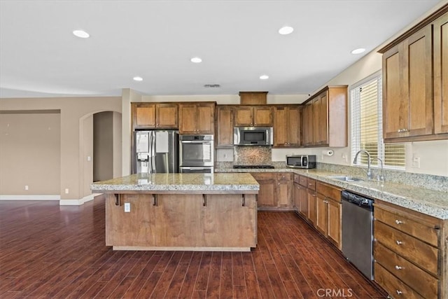 kitchen featuring dark wood-style floors, a kitchen island, arched walkways, a sink, and stainless steel appliances