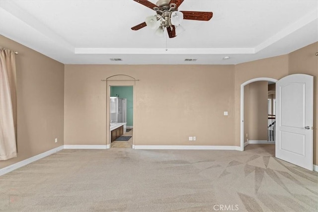 spare room featuring a tray ceiling, visible vents, arched walkways, and baseboards