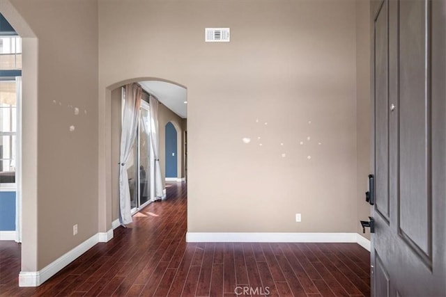 unfurnished room featuring baseboards, dark wood-style floors, visible vents, and arched walkways