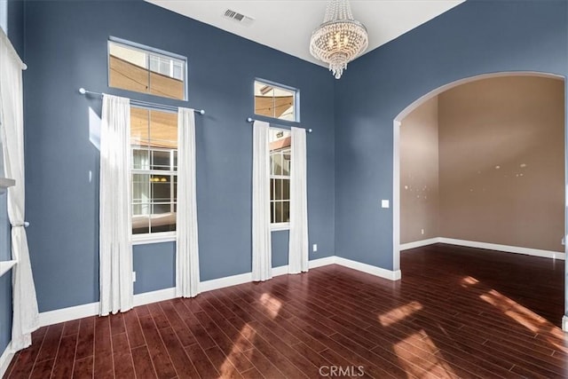 spare room featuring a wealth of natural light, arched walkways, a chandelier, and wood finished floors