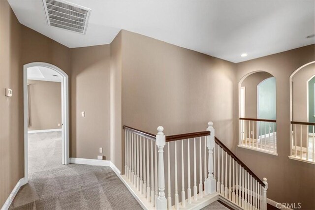 hall featuring visible vents, an upstairs landing, carpet floors, arched walkways, and baseboards