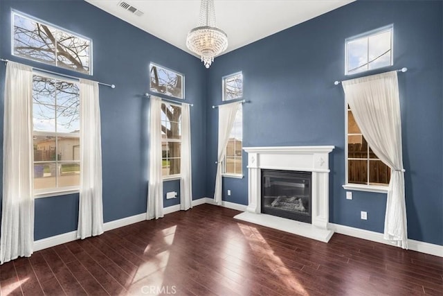 unfurnished living room with wood finished floors, visible vents, baseboards, a glass covered fireplace, and a chandelier