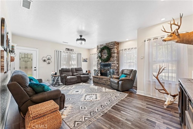 living area with visible vents, a healthy amount of sunlight, a stone fireplace, and dark wood-style flooring