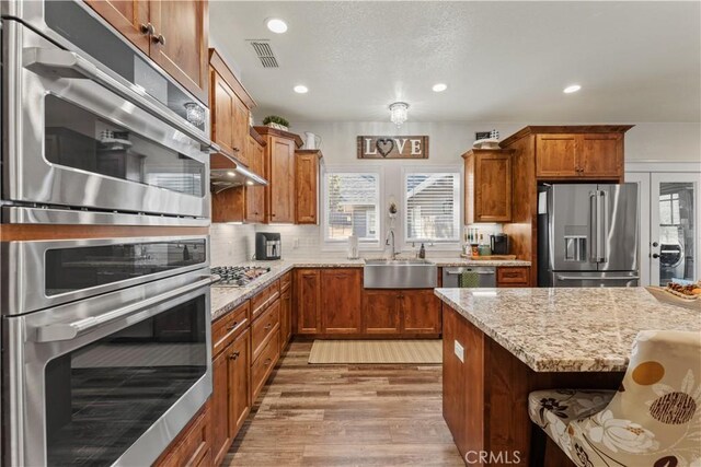 kitchen featuring brown cabinetry, visible vents, light stone countertops, a sink, and stainless steel appliances