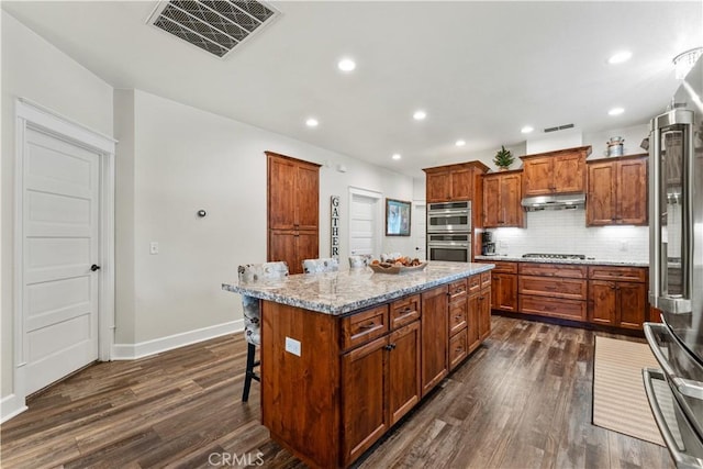 kitchen featuring under cabinet range hood, visible vents, appliances with stainless steel finishes, and dark wood-style floors