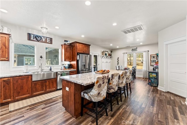 kitchen featuring visible vents, a breakfast bar, dark wood-style floors, stainless steel appliances, and a sink