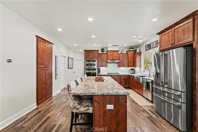 kitchen featuring tasteful backsplash, a kitchen island, under cabinet range hood, stainless steel appliances, and a sink