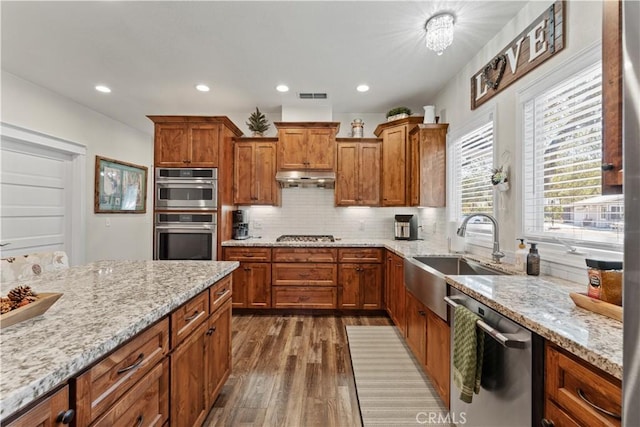 kitchen featuring visible vents, brown cabinets, a sink, under cabinet range hood, and stainless steel appliances