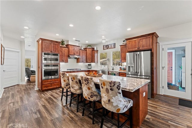 kitchen featuring backsplash, a kitchen island, under cabinet range hood, dark wood-style floors, and stainless steel appliances