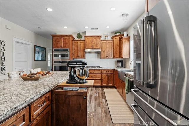 kitchen with a sink, appliances with stainless steel finishes, brown cabinetry, and under cabinet range hood