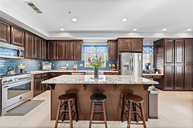 kitchen with visible vents, a kitchen island, dark brown cabinetry, a breakfast bar area, and appliances with stainless steel finishes