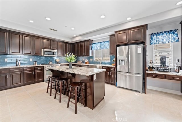 kitchen with light tile patterned floors, visible vents, stainless steel appliances, dark brown cabinets, and a kitchen bar