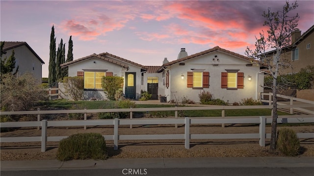 mediterranean / spanish-style home with a tile roof, a chimney, a fenced front yard, and stucco siding