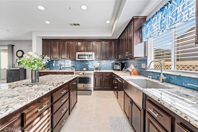 kitchen with light stone counters, light tile patterned flooring, stainless steel appliances, dark brown cabinets, and tasteful backsplash