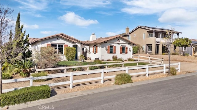 mediterranean / spanish-style house featuring a fenced front yard, stucco siding, a tiled roof, and a chimney