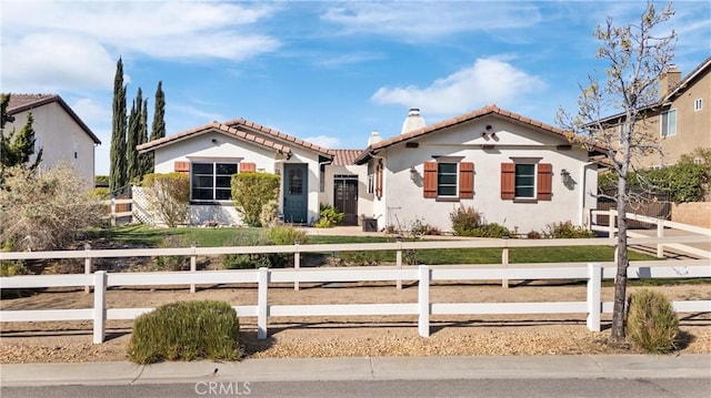 mediterranean / spanish house featuring a tile roof, a chimney, a fenced front yard, and stucco siding